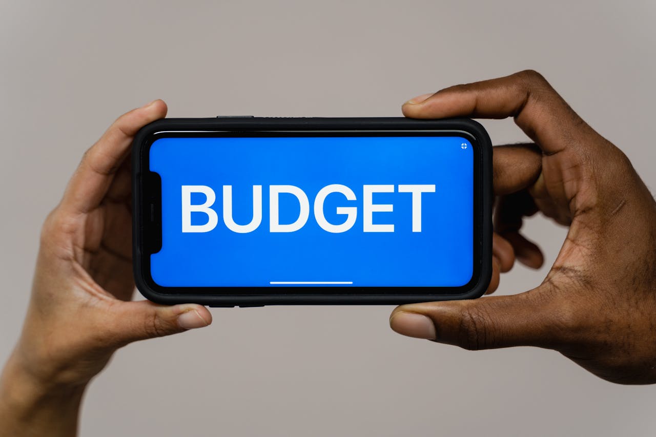 Two hands hold a smartphone displaying the word budget on a blue screen, symbolizing financial planning.